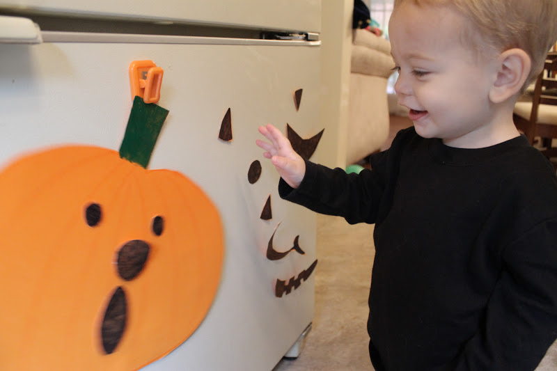 Toddler copying pumpkin facial expressions playing on a fridge with magnet pieces.