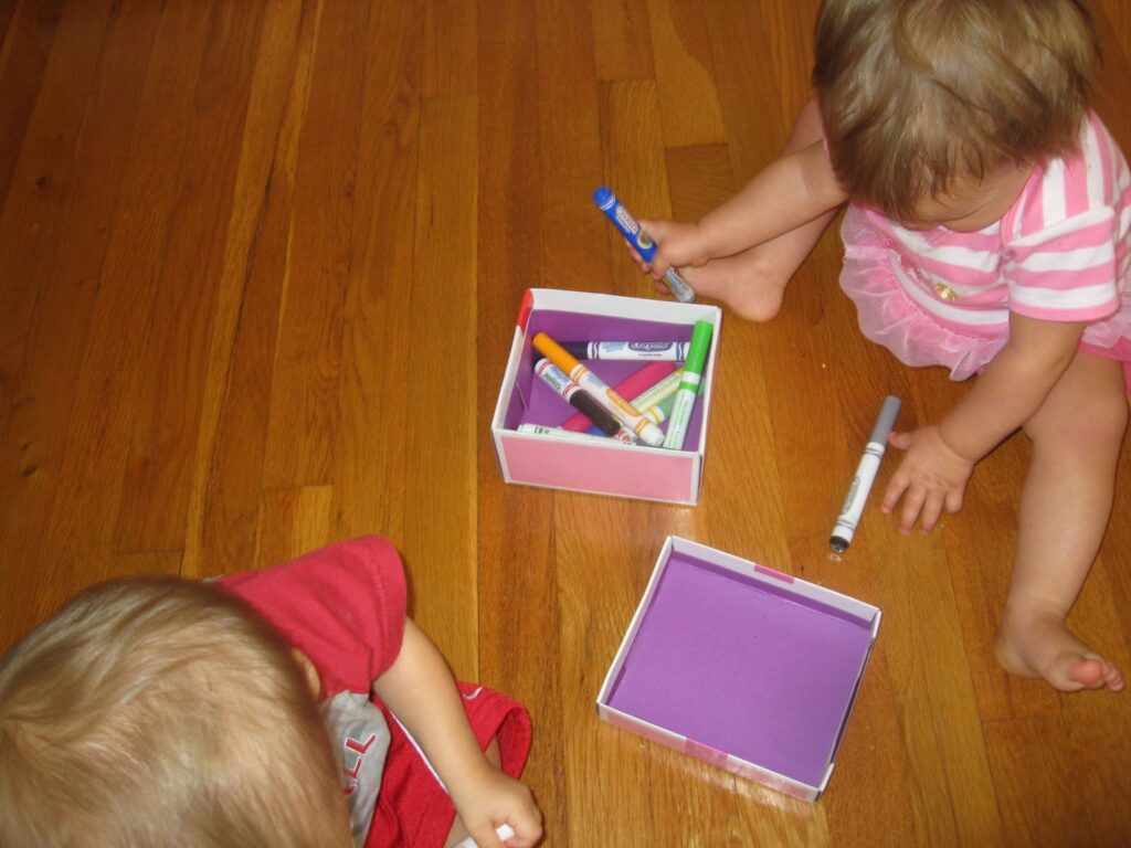 Babies putting markers into a cardboard box
