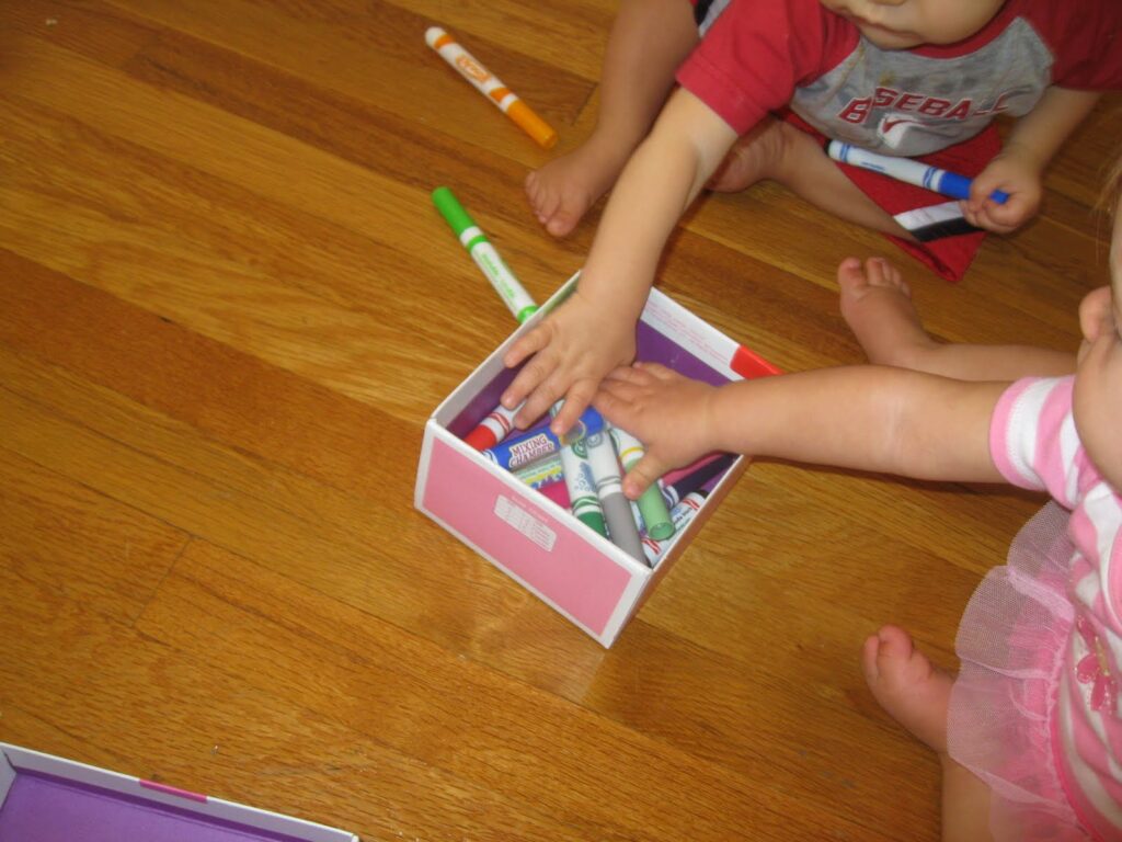 Babies reaching into a cardboard box to grab colorful markers