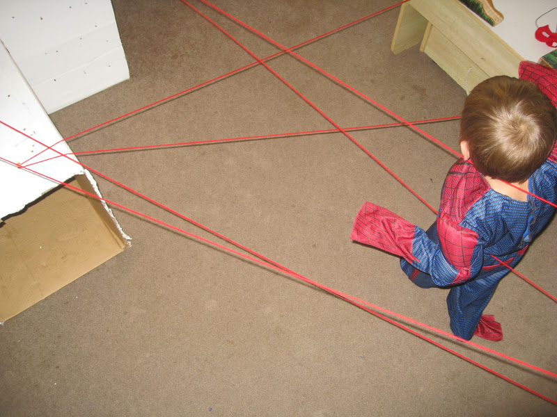 Child in Spiderman costume moving through a spider web obstacle course.