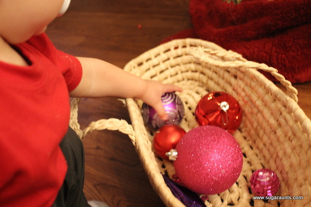 Small child reaching for an ornament in a Christmas ornament sensory bin in a basket