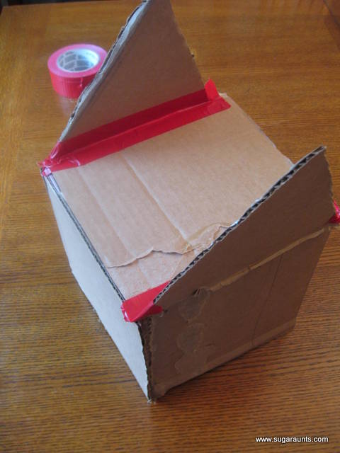 Tape triangle pieces to the cardboard house.