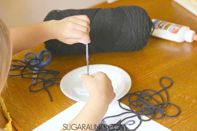 Child dipping black yarn into glue to stick to the bat printable